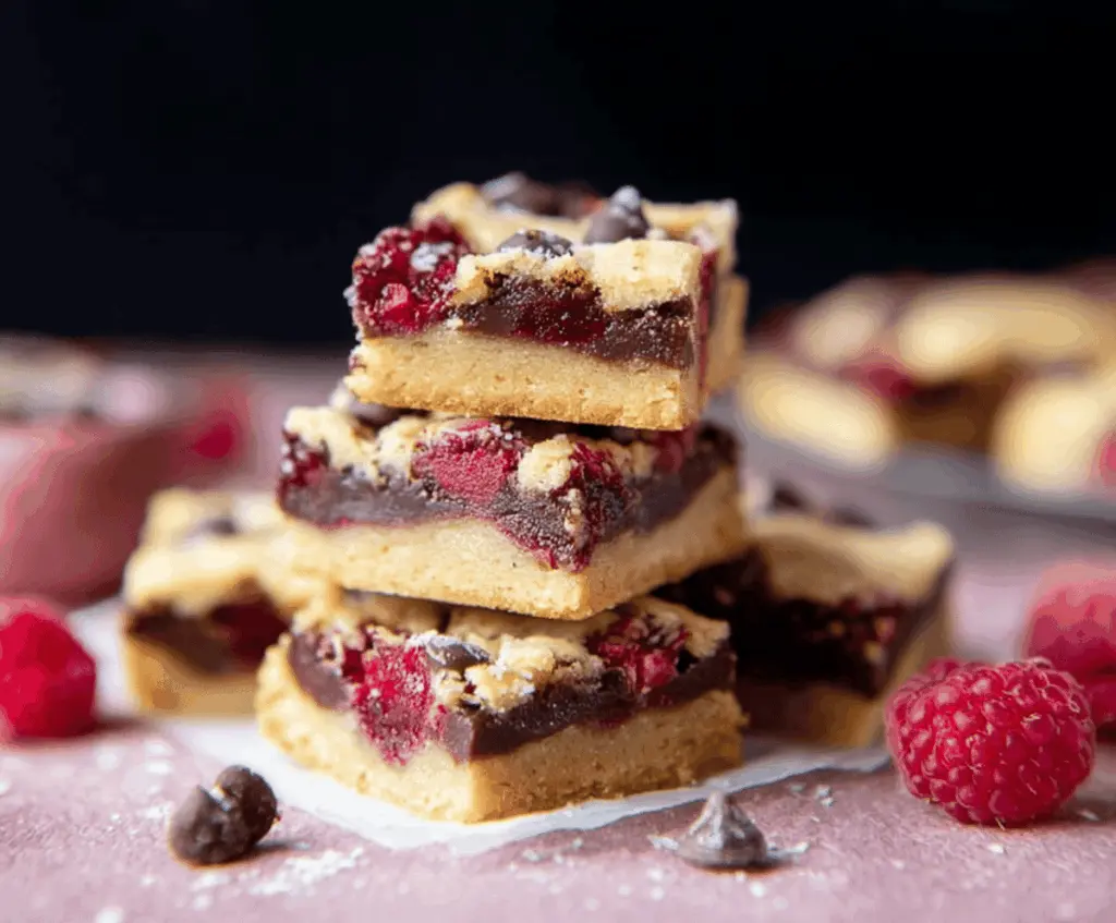 Delicious Raspberry Chocolate Chip Shortbread Bars on a white platter, showcasing vibrant red raspberries and chocolate chips in a golden shortbread crust.