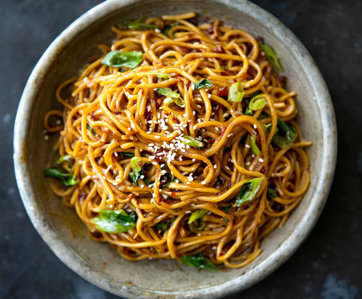Delicious Asian garlic noodles garnished with vegetables and herbs, served on a plate.