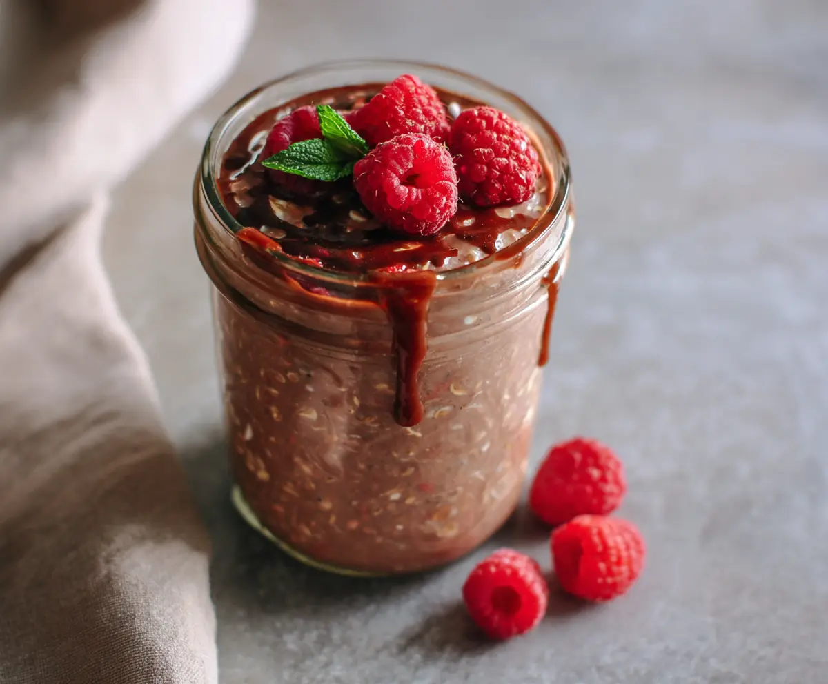 Creamy chocolate raspberry overnight oats in a glass jar with fresh raspberries and chocolate shavings on top.