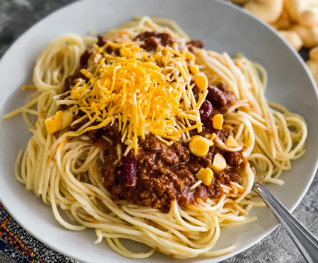 A plate of Cincinnati chili spaghetti topped with shredded cheese and chopped onions.