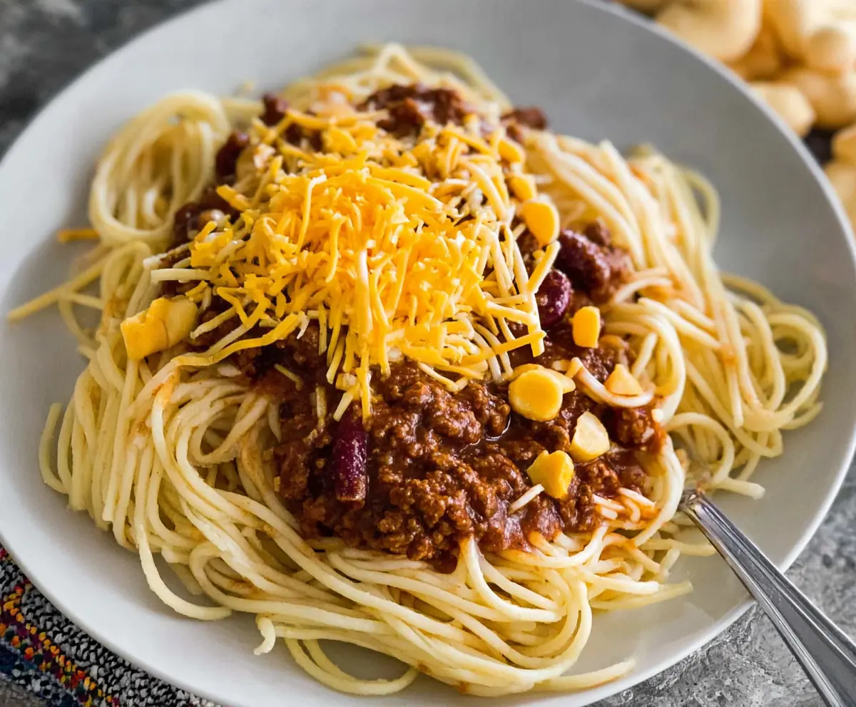 A plate of Cincinnati chili spaghetti topped with shredded cheese and chopped onions.