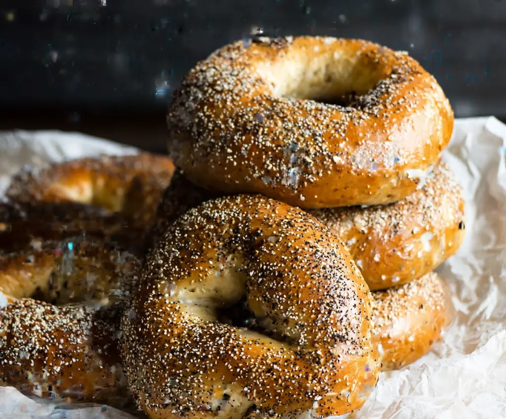 Golden New York Style Sourdough Discard Bagels topped with sesame seeds on a baking tray.