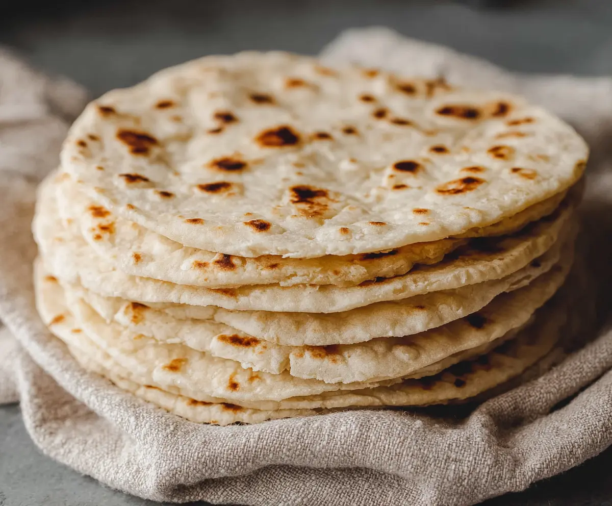 Homemade sourdough discard tortillas on a wooden surface, showcasing their soft, flexible texture and rustic appearance.