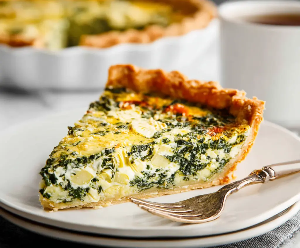 Delicious spinach and artichoke quiche with golden crust served hot on a white plate.